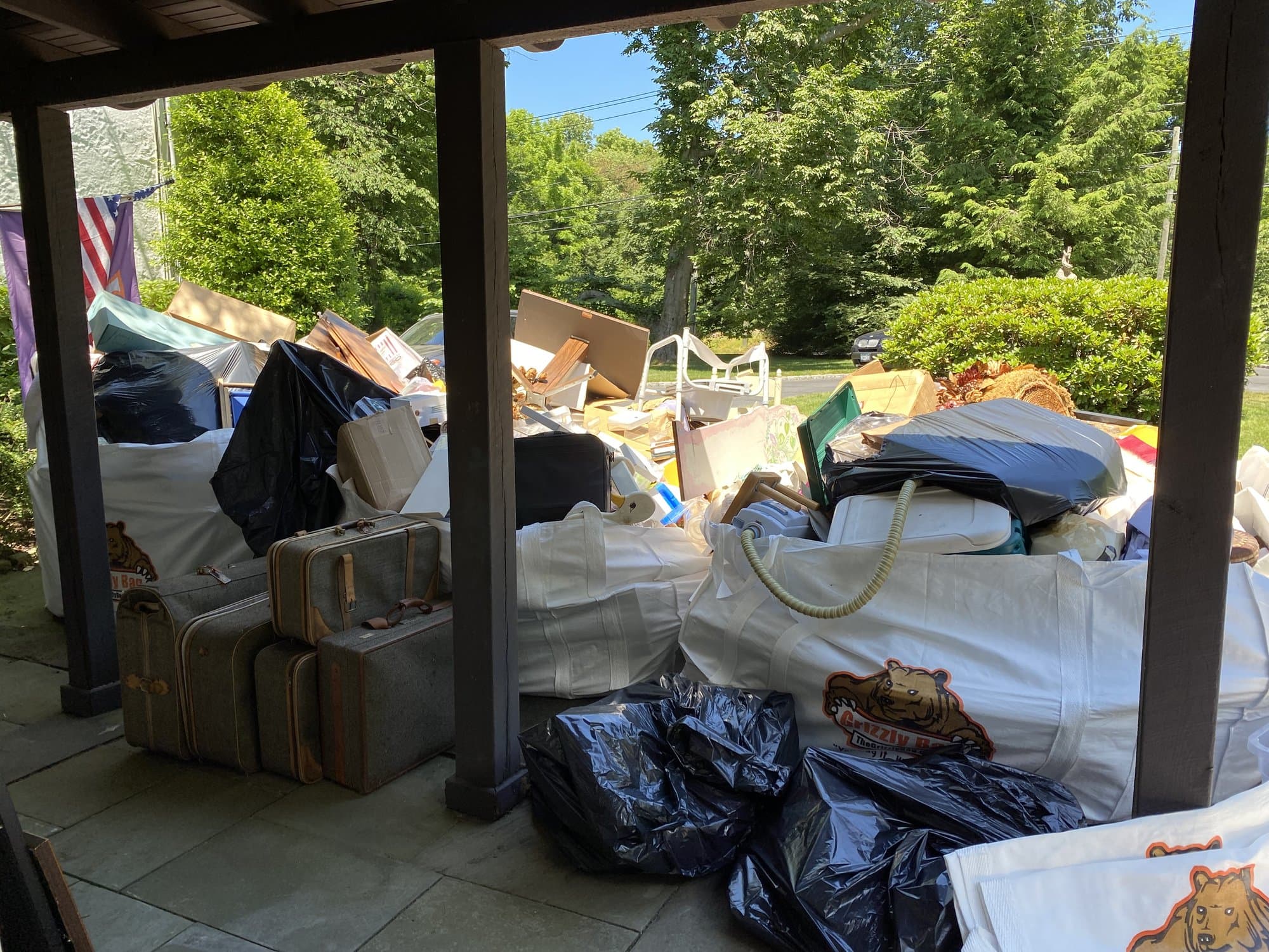Pre-listing cleanout staging at a Darien, CT home — household items and luggage piled under a covered porch ready for removal